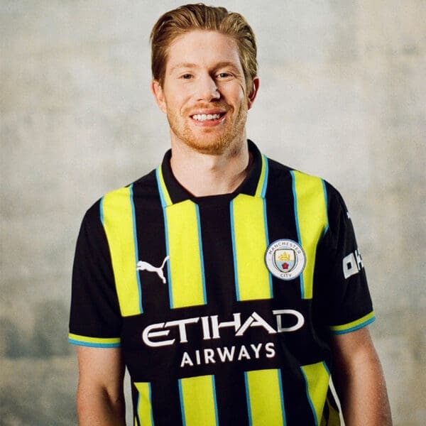 Man in Manchester City jersey smiling.