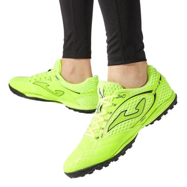 Neon green Joma soccer cleats on feet.