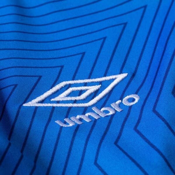 Embroidered Umbro logo on blue fabric.